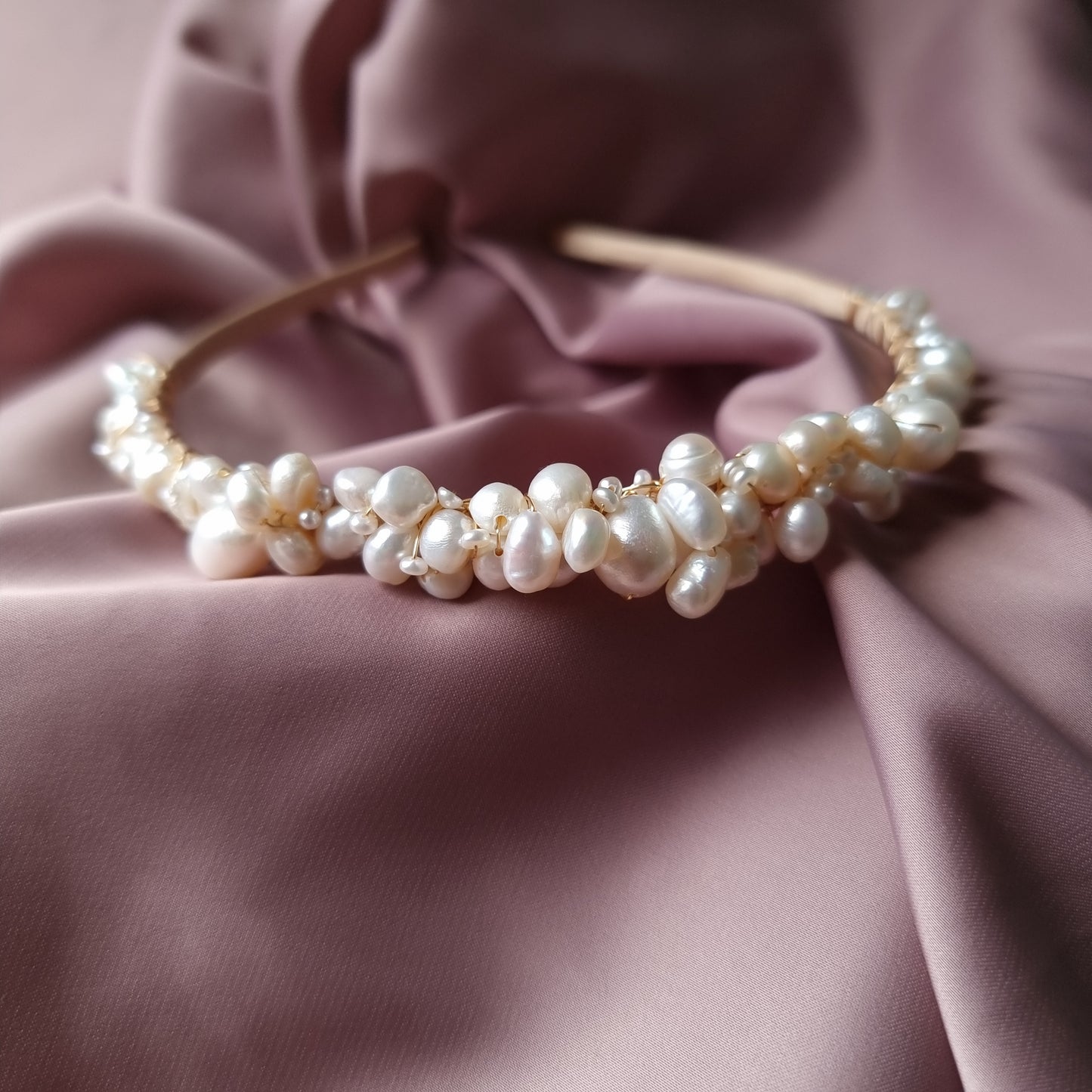 A bridal tiara with a blend of freshwater pearls in various sizes, displayed on a pink fabric background.