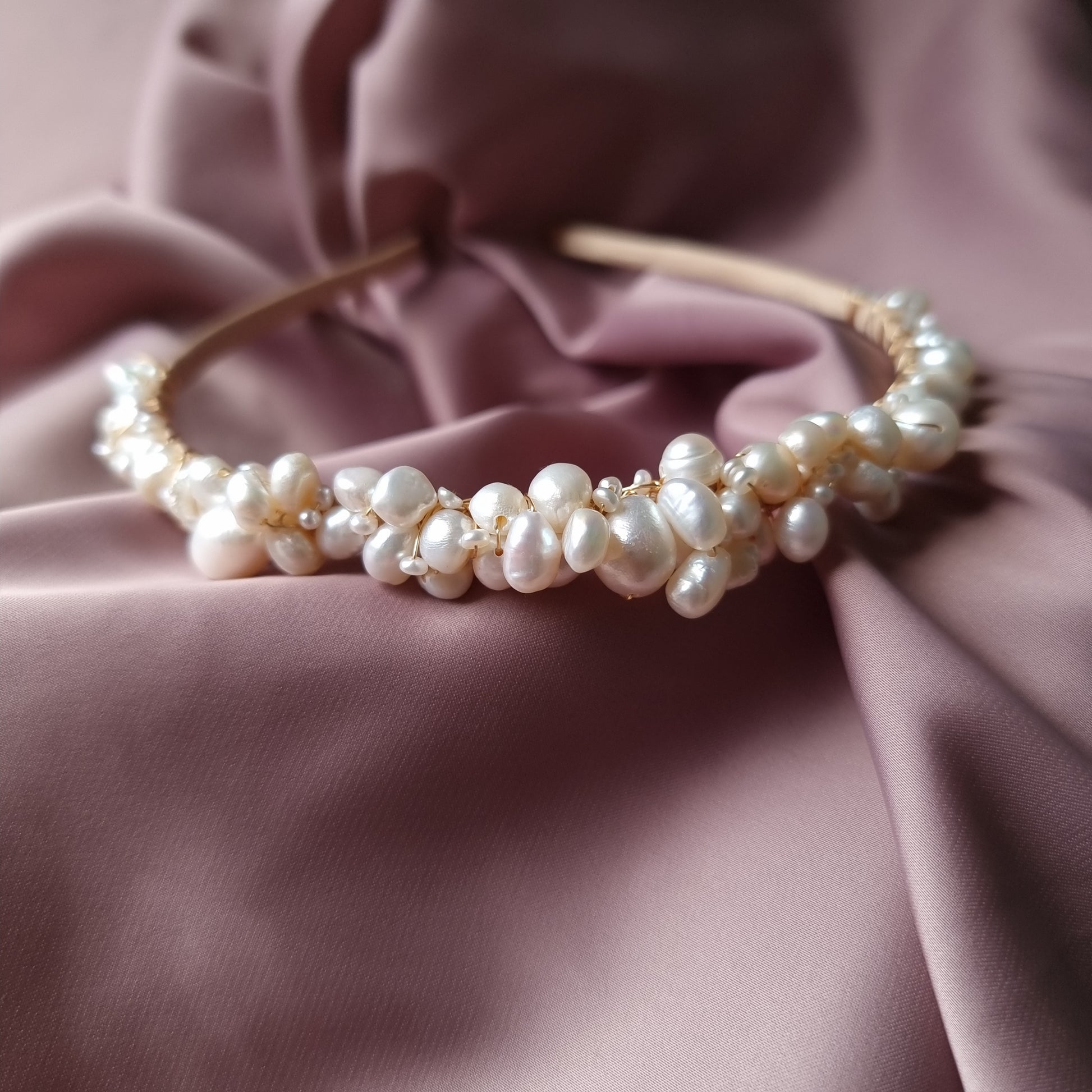 A bridal tiara with a blend of freshwater pearls in various sizes, displayed on a pink fabric background.